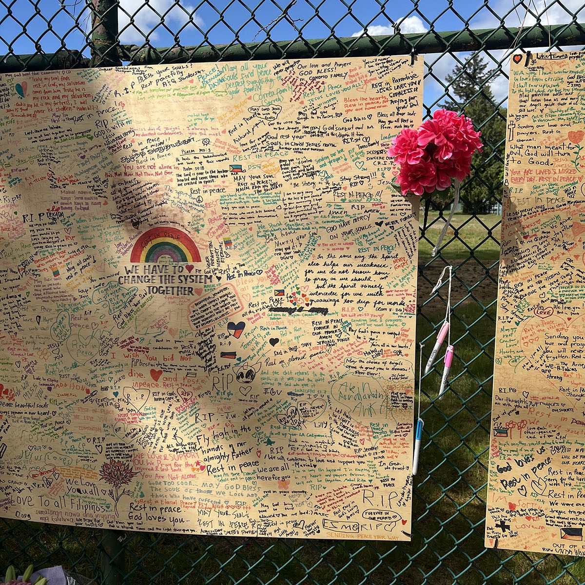 Hand written messages of hope and sympathy posted on a board alongside flowers against school field fence on East 43rd Avenue.