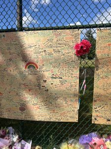 Hand written messages of hope and sympathy posted on a board alongside flowers against school field fence on East 43rd Avenue.