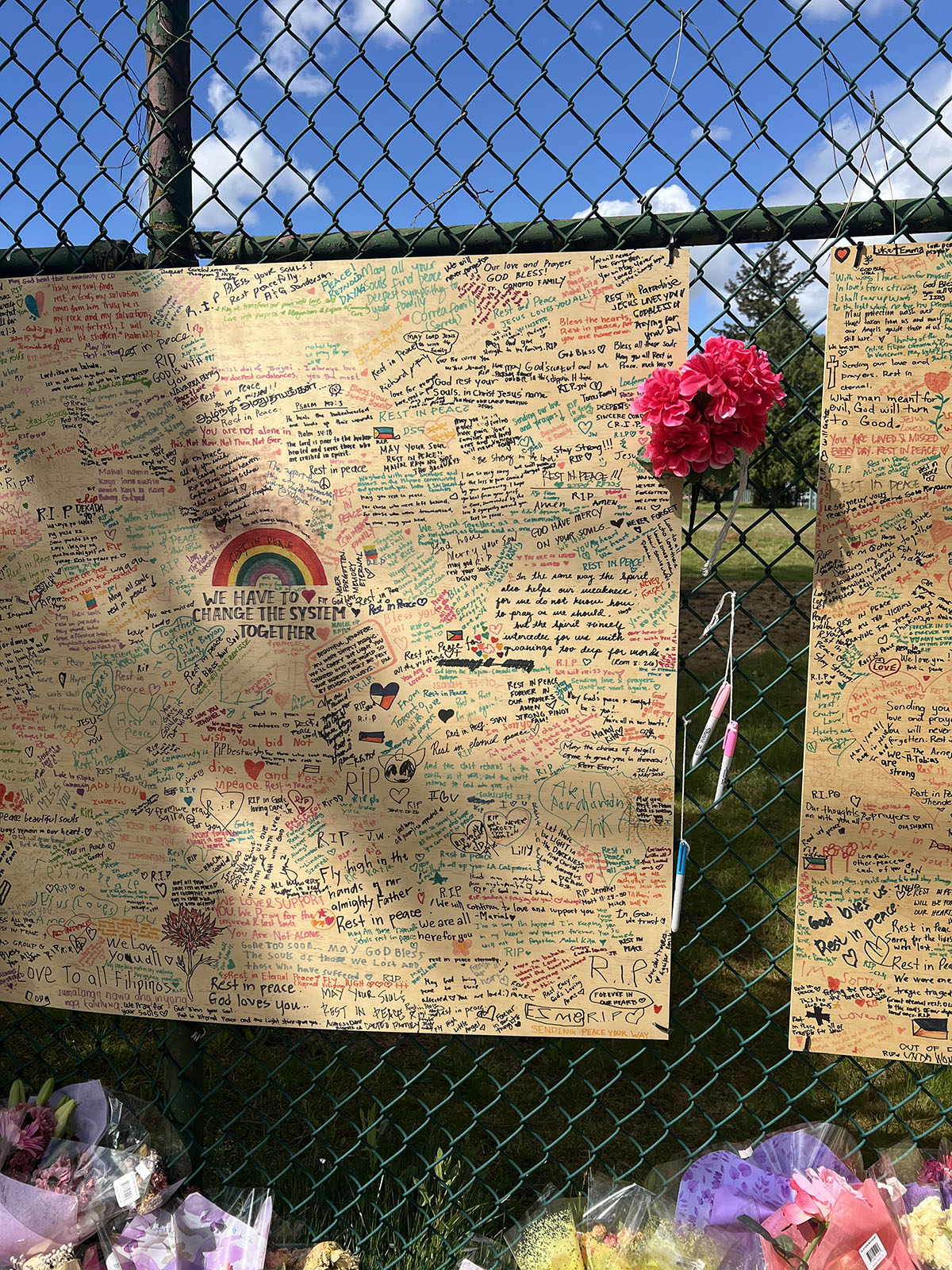 Hand written messages of hope and sympathy posted on a board alongside flowers against school field fence on East 43rd Avenue.